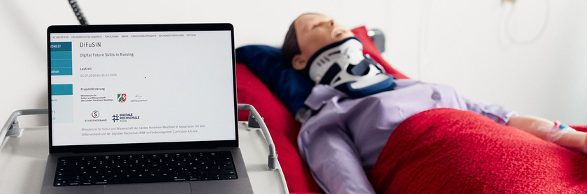 Ein Laptop zeigt die Projektseite des Projektes DiFuSiN, daneben liegt eine medizinische Puppe in einem Krankenhausbett
