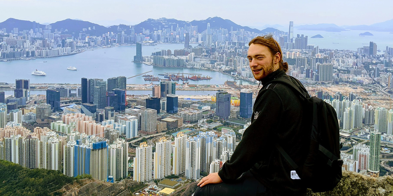 Moritz Mey sitzt auf einem Berg vor dem Panorama Hongkongs